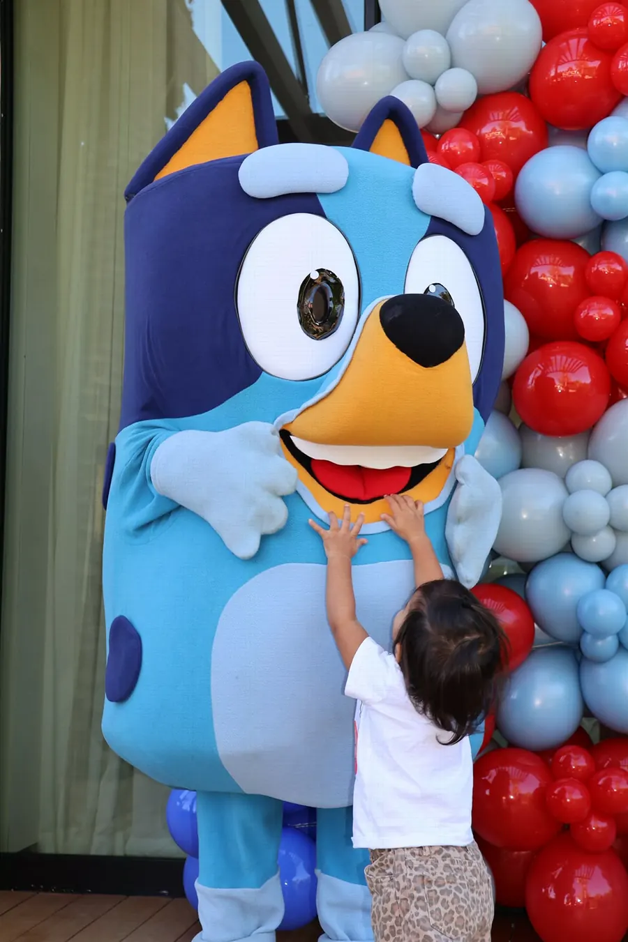 Toddler reaching up to a Bluey character at a party, photographed by Lihi Matzri