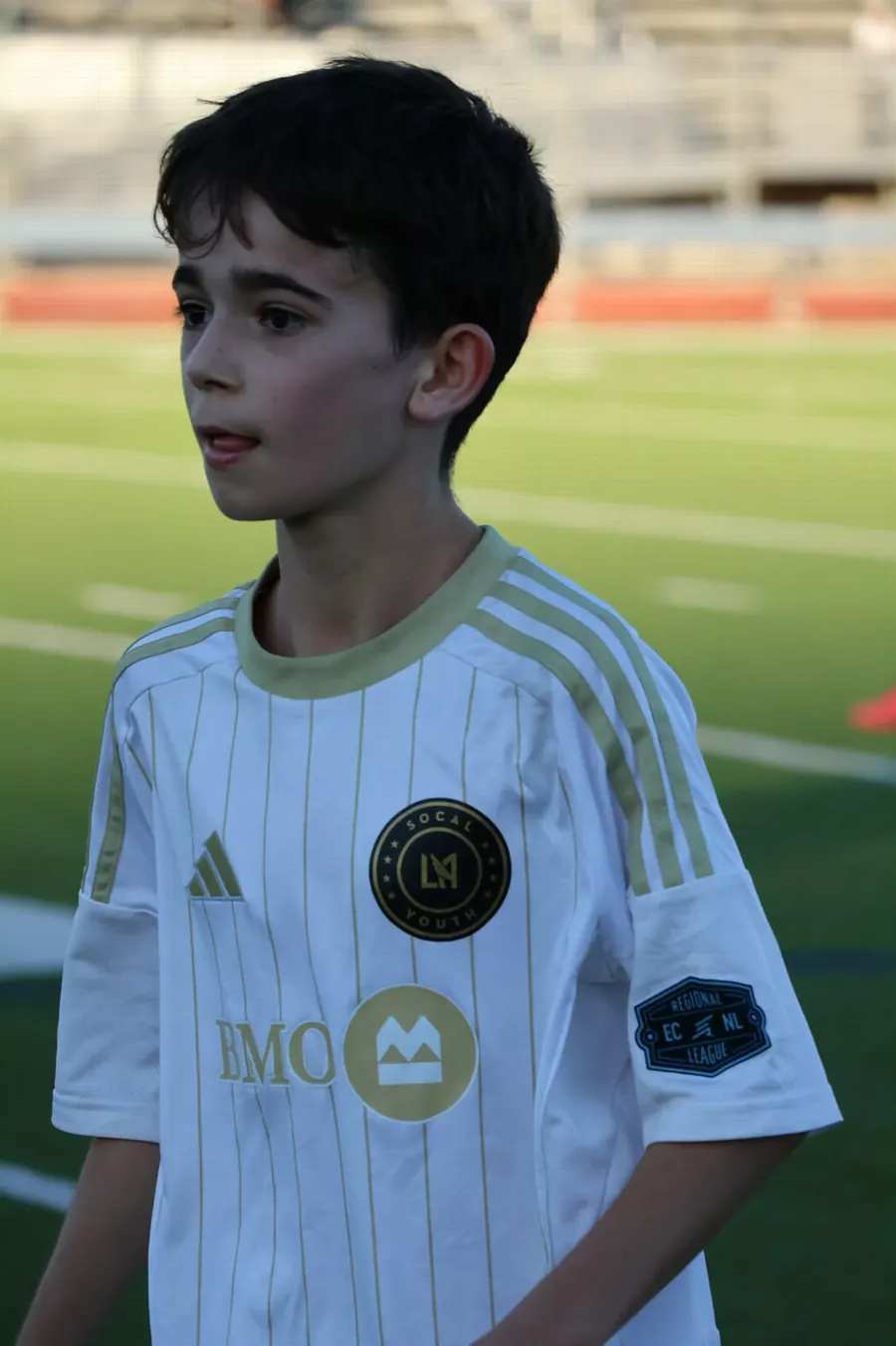 Close portrait of a young soccer player in a white and gold kit on the field, photographed by Lihi Matzri